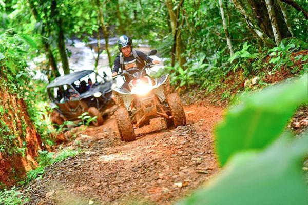 ATV rider splashing through a muddy forest trail near Jaco