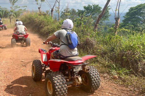 Riders on ATVs following a dirt road through the Jaco countryside