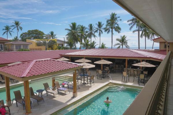 Second-floor view of both Hotel Cocal pools with a glimpse of the ocean and palm trees