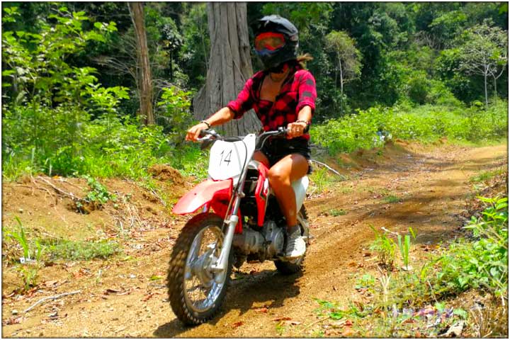 Girl in lumber jacket driving mini dirt bike in costa rica