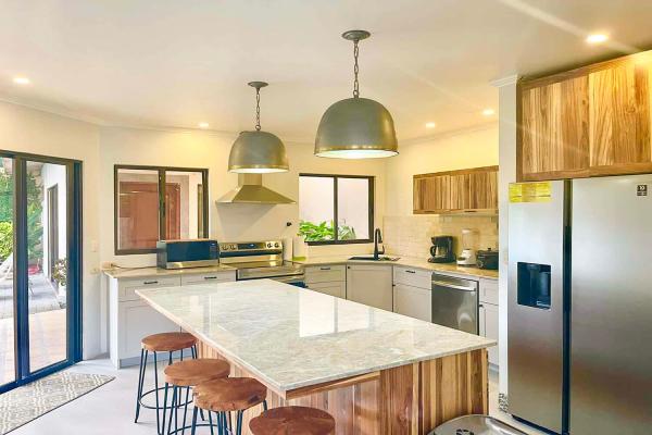 Main kitchen at Casa Cuatro Jaco with white cabinets, granite island, and living room with sofa and TV