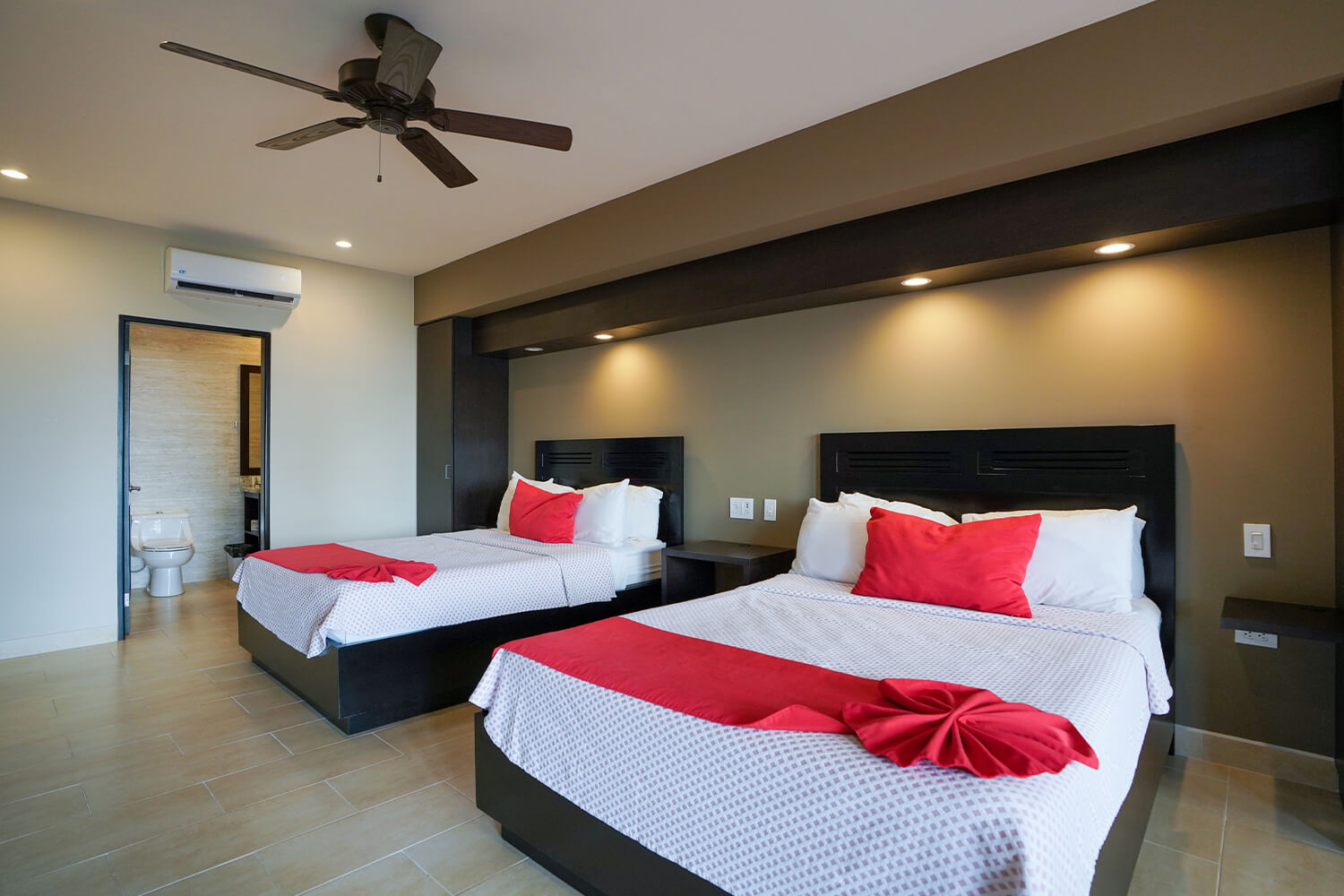 Room with two queen beds and red accents at Hotel Cocal, bathroom door open
