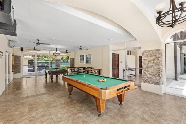 Two pool tables beneath an arched ceiling with iron chandelier and stone column anchoring the billiards room.