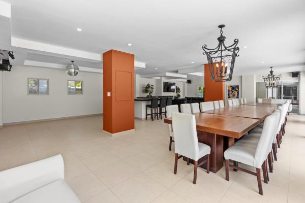 Long wooden dining table with white chairs and the burnt orange accent column framing the doorway in this open layout