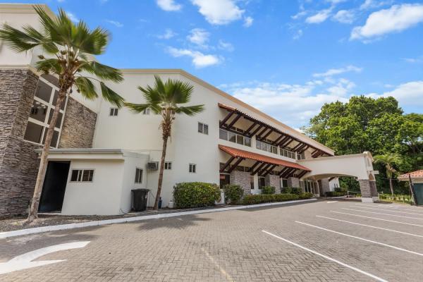 Front paved driveway and parking area with tall palms and the long two-story stucco property building running alongside