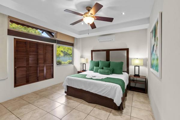 King bed with carved dark wood headboard and green accent linens beneath a ceiling fan in bedroom one at Rancho de Sueños