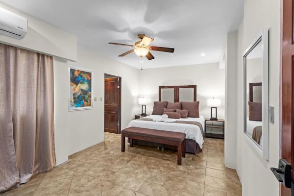 King bedroom 4 with cool tile floors wood headboard ceiling fan and en-suite door at this welcoming Pacific coast home