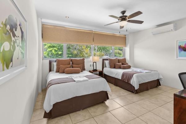 Two queen bedroom 8 with brown linen accents bedside lamps and a large window overlooking tropical garden foliage.
