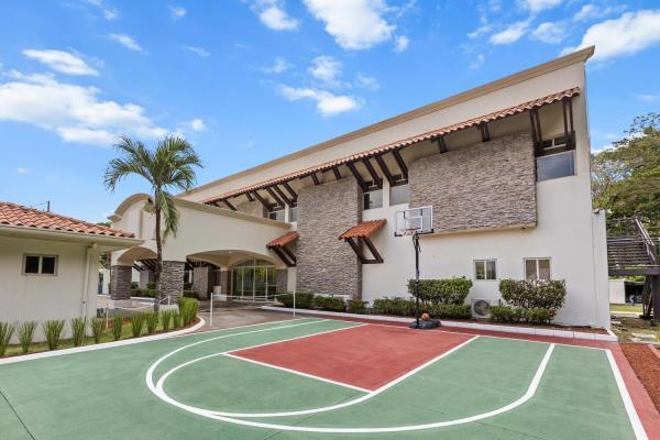 Side angle of the property half basketball court with red and green surface palms and stone villa walls in view
