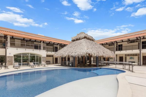 Stunning overhead view of the curved lagoon-style swimming pool with central palapa surrounded by the building wings
