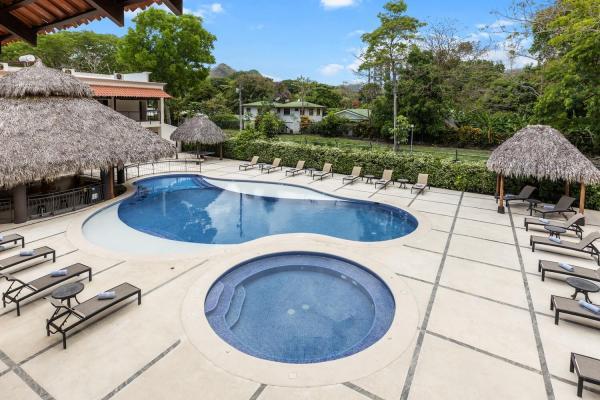 Different view of the kidney pool and round hot tub showing palapa shade structures and rows of lounge chairs nearby