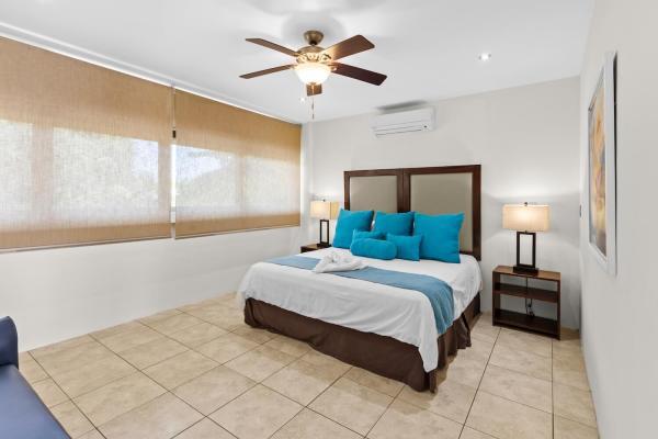 King bedroom 15 with blue pillow accents wood bench at foot of bed ceiling fan and natural window light from outside