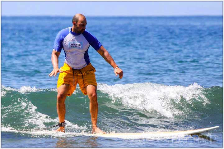 Guy with ornage board shorts on surfboard