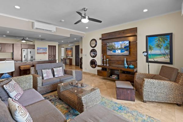 Open living room at The Palms 1002 with wicker sofas, wall-mounted TV and tropical artwork
