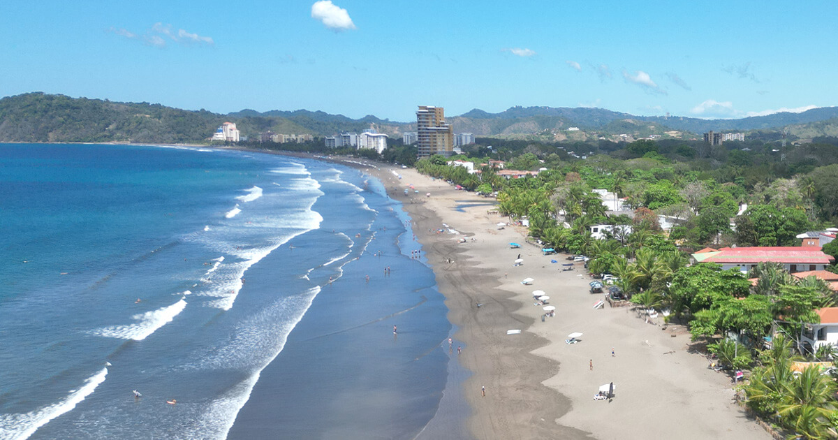 Wide cinnamon-sand beach at Playa Jaco with green mountains in the background, Costa Rica