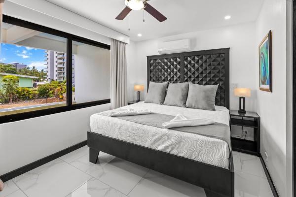 1 King Bed Serene king bedroom with tropical palm views through large windows and a dark tufted headboard, Jaco Beach
