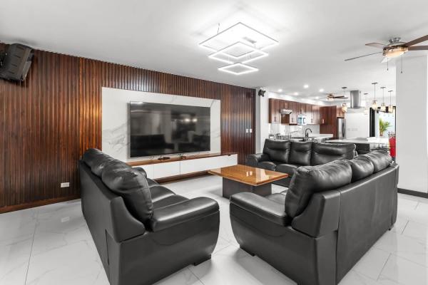 Modern open-plan living space with warm wood wall panels, sectional seating, and elegant hanging pendant lights