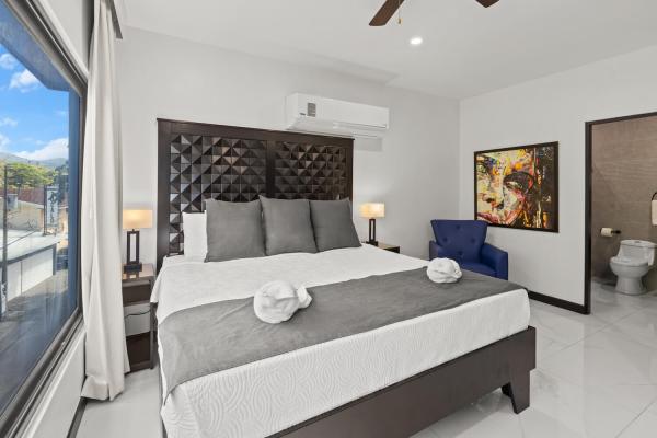 King bedroom with city and mountain view window, blue accent armchair and dark wood headboard, Jaco Beach