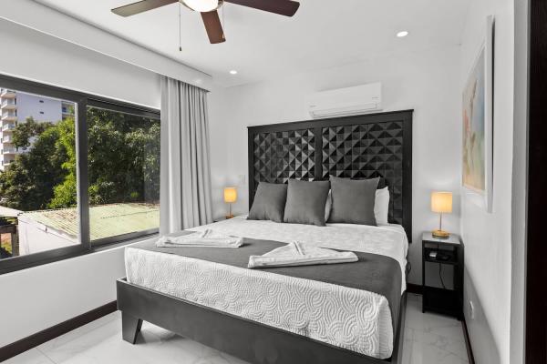 Bright king bedroom with large oversized windows framing outdoor treetop and street views in central Jaco