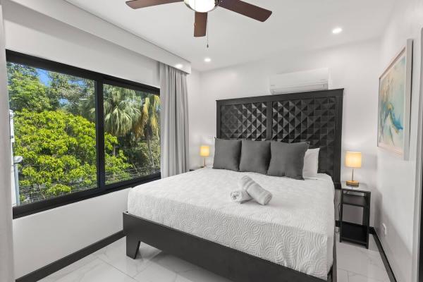 King bedroom with a large window overlooking tropical palms and garden below with ceiling fan visible