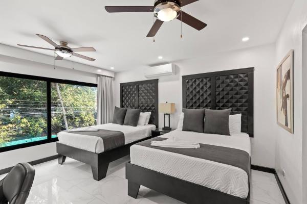 Twin queen bedroom with tropical garden view through large windows and dual ceiling fans, Costa Rica vacation villa