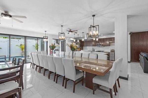 Long dining table with white upholstered chairs and pendant chandelier with pool view, central Jaco