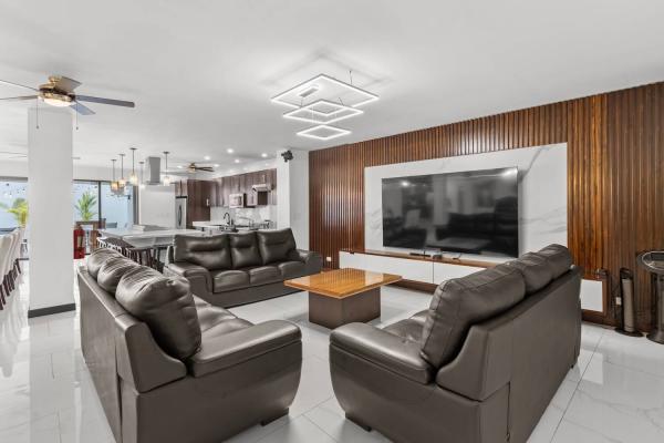 Spacious lounge area with leather sofas, large wall-mounted TV and the open-plan gourmet kitchen in view